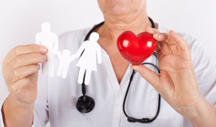 Médecin avec stéthoscope autour du cou tenant des personnages en papier découpé dans une main, et un coeur en bois rouge de l'autre main