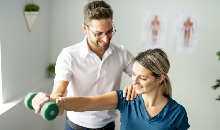 Séance de kiné : un praticien aide sa patiente à réaliser un exercice à l'aide d'une haltère