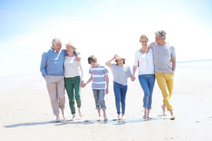 Grands parents, parents et petits enfants qui marchent sur une plage avec le sourire