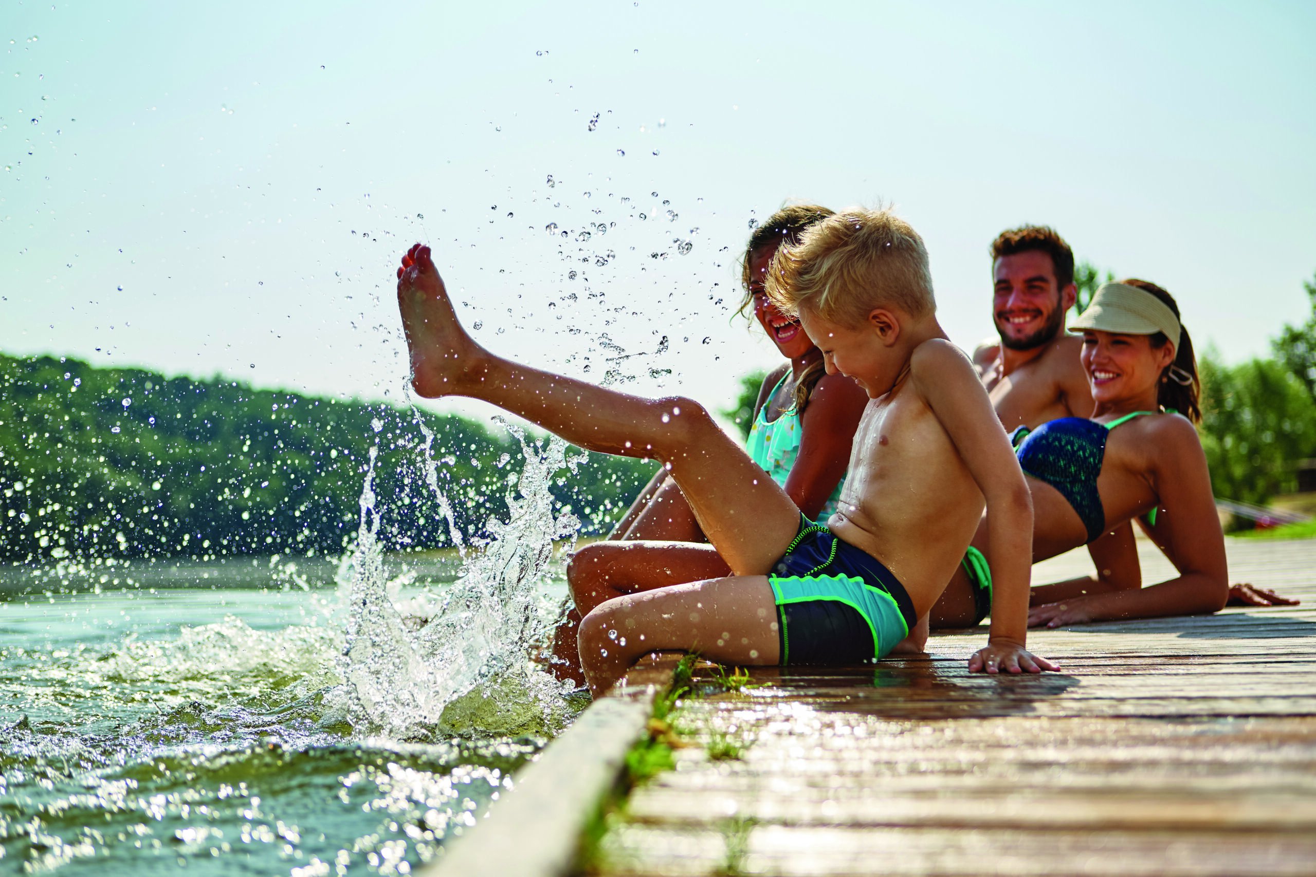 Familie am See badet glücklich mit Füßen im Wasser im Sommer